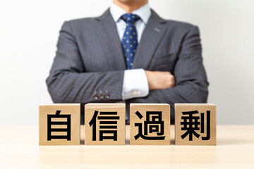 Obraz premium 「自信過剰」と書かれたブロックと腕組みをするビジネスマン