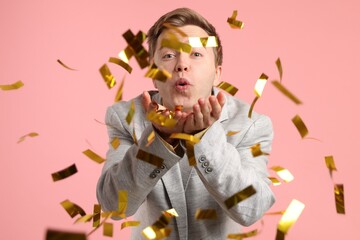 Happy young man blowing confetti on pink background