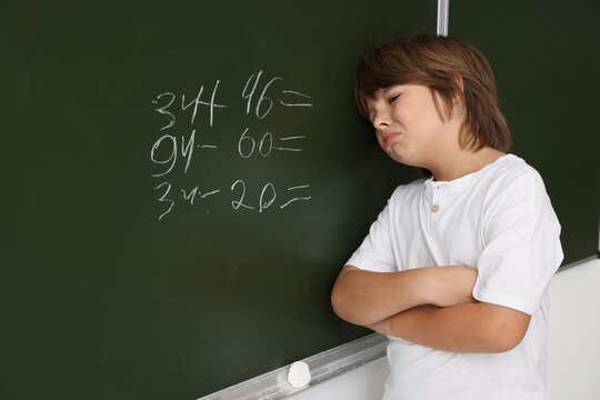 Back to school. Upset boy near chalkboard with math assignment indoors