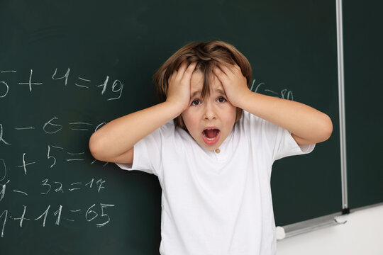 Back to school. Shocked boy near chalkboard with math assignment indoors