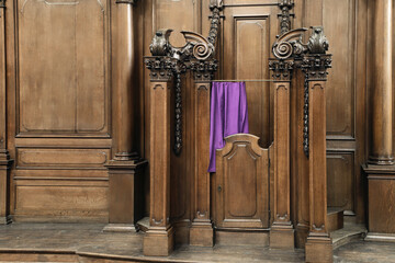 Wooden confessional with carved columns and a purple curtain symbolizing penance, set against ornate wooden paneling. St. Andrew's Church in Antwerp
