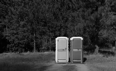 Black and white image of portable restrooms next to each other.