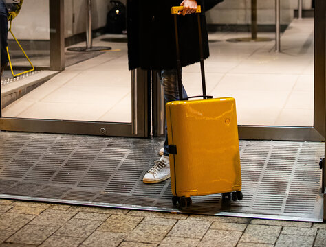 A traveler with a bright suitcase at a doorway.