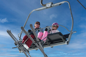Two females us a ski lift to get themselves and their ski equipment to the top of the mountain and be able to enjoy the sport of skiing down again on the snow on a cold winters day.