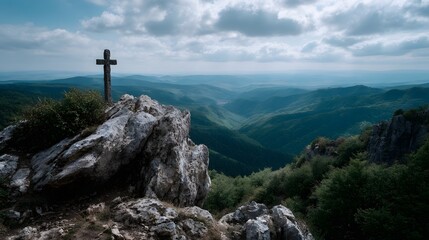 Obraz premium A wooden cross on a rocky mountain peak overlooks a vast green valley under a dramatic cloudy sky