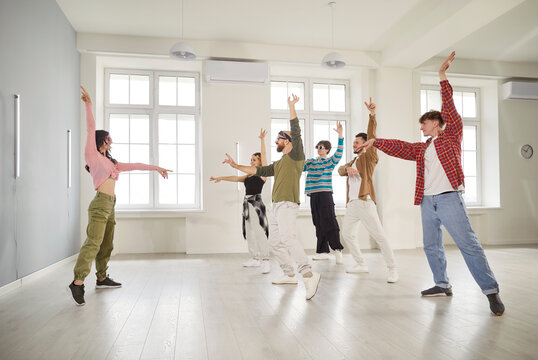 Smiling young people training modern dance moves together in studio with female choreographer. Group of men and women doing dance workout in choreography class. Sport and active lifestyle concept.
