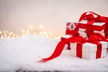 Festive white gift box tied with a red ribbon, resting on snow with blurred golden lights in the...