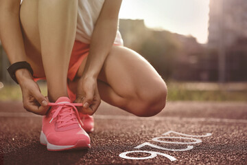 New Year. Woman tying shoelaces near numbers 2026 on road at stadium, closeup