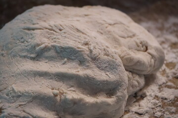 A loaf of raw pizza dough sitting on a granite countertop covered in flour.
