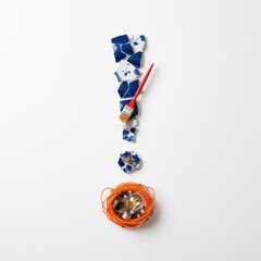 Colorful ceramic shards arranged in an exclamation mark shape, with a paintbrush and orange cord, creating a visually striking and artistic composition for creative projects