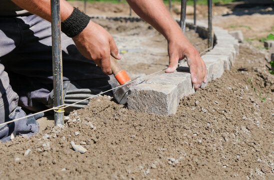 Landschaftsg&auml;rtner bei der Arbeit im Detail &ndash; pr&auml;zise Handarbeit im Gartenbau mit Fokus auf Steine, Werkzeug und Struktur. Selektive Sch&auml;rfe, viel Copy Space