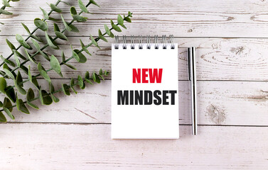 NEW MINDSET text on white notepad with pen and green leaves on wooden background