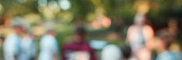 Blurred outdoor gathering with mixed-gender and race individuals in a natural setting.