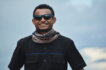 Smiling Asia Papua Man Wearing Sunglasses and Scarf Looking at Camera Outdoors