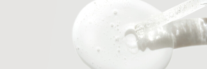 Close-up of a clear liquid serum with bubbles and dropper on a light background.