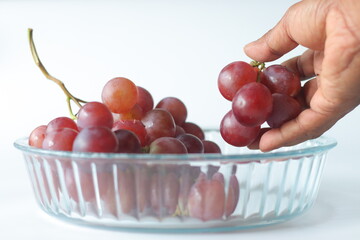 A hand reaching to a glass bowl of Red table grapes or Red Globe, Crimson Seedless or Flame Seedless