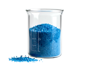 Clear glass beaker filled with textured blue granules; some scattered on the table against a stark black background