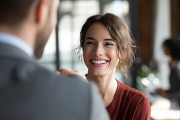 Smiling woman with brown hair in casual attire engages in conversation with a man in a suit, showcasing a warm and friendly atmosphere in a modern office setting