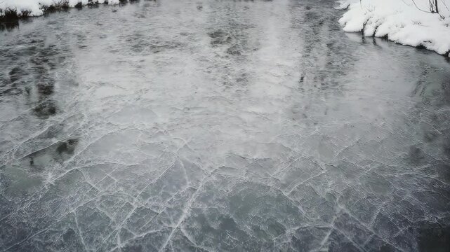 A cracked icy pond surface with snow on the banks, reflecting the sky