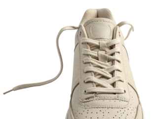 Close up of a creamy tan sneaker, showing laces, perforations, and padding against a black background