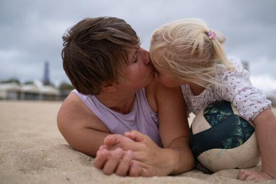Woman in sportswear relaxing on the beach with her daughter on the sand. 