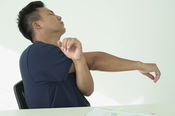 Young asian businessman is suffering pain on wrist, finger and arm, arthritis inflammation while working and he is massaging himself and doing exercise with his hands to relax and to relieve pain.
