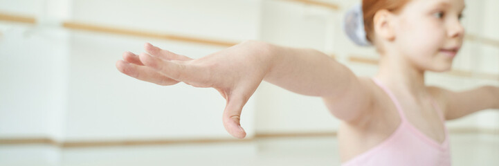 Young caucasian female child practicing ballet in dance studio with arm outstretched. © elenavolf