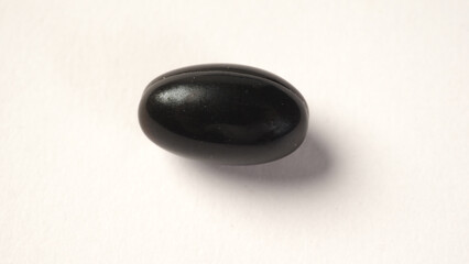 A close up of black capsule or vitamin on white background.