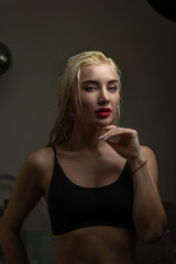 Blonde woman with wet hair poses elegantly in a dimly lit room, showcasing beauty and confidence, with soft shadows enhancing her features and creating a captivating atmosphere