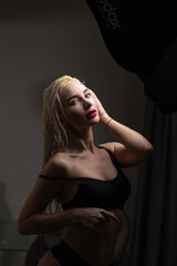 Blonde woman with wet hair poses elegantly in a dimly lit room, showcasing beauty and confidence, with soft shadows enhancing her features and creating a captivating atmosphere