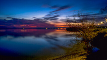 Dramatic sunset over calm lakeside with silhouettes of bare trees