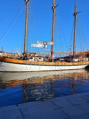 Classic wooden sailboat turned into a floating restaurant, shining under bright sunlight with blue water reflections. Nautical lifestyle and seaside leisure mood.с