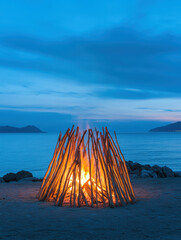 Bonfire on the beach with water reflections at twilight near coastal landscape