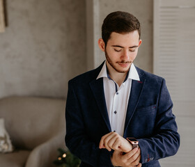 Portrait of a handsome young man in a stylish blue suit jacket and white shirt adjusting his smartwatch, getting ready for a Christmas party or holiday business event