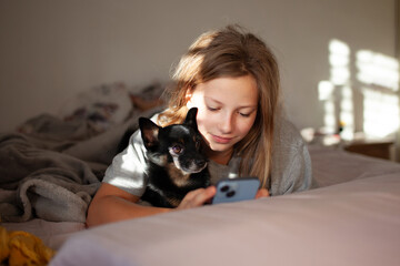 Morning moment — preteen girl with her chihuahua dog in bed using smartphone