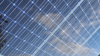 Solar panels reflecting clouds in bright blue sky  