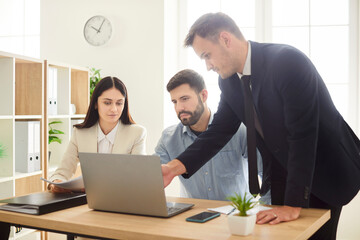 Company employees talking with colleagues on workplace in office looking at laptop monitor screen...