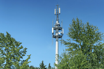 Obraz premium Tower stands tall against clear blue sky with trees below, symbolizing modern communication technology and connectivity