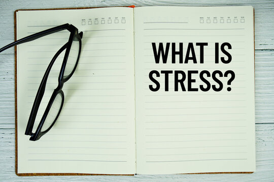 Notepad with message "What Is Stress?" and eyeglass on wooden background