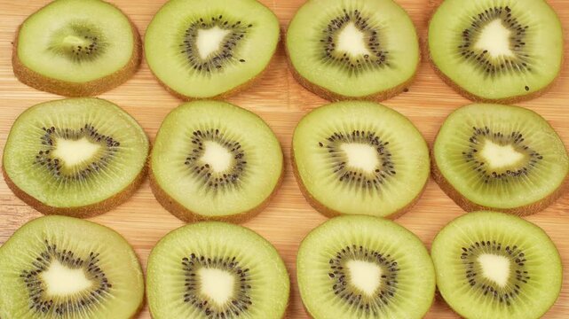 Static top-down (flat lay) shot of fresh green kiwi slices arranged in a neat pattern on a wooden cutting board. Food background concept.