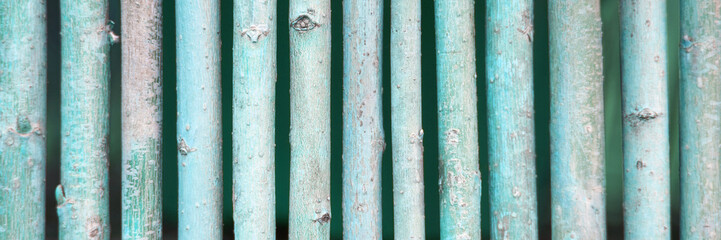 Weathered green wooden fence close-up texture with vertical sticks and rustic surface.