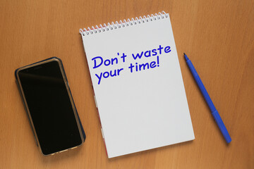 Open notebook with inscription: Don’t waste your time, mobile phone and marker on table