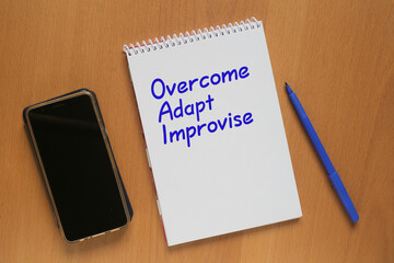 Open notebook with inscription: Overcome, Adapt; Improvise, mobile phone and marker on table