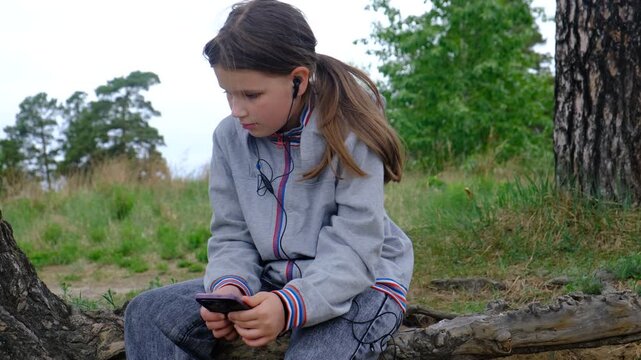 Teenager girl looks pensive, perhaps even a bit sad. Introspection, contemplation, wearing headphone, listening music, enjoy spending time in parklands