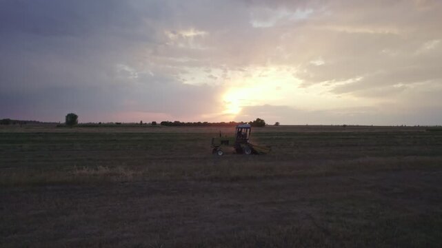 Aerial view on a tractor that collects hay in rows with a disc rake. Farmer stores fodder for cattle in summer season.
Tractor Working on Farm at Sunset Time.
