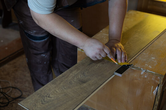 A man lays new laminate flooring, carefully measuring and marking a wooden plank with a ruler and pencil. This man prepares laminate flooring for proper installation during a home renovation.