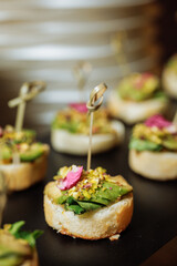 Elegant avocado canapes with pistachios and edible flower on black serving tray