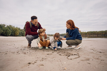 Happy family writing in sand by lake in autumn day.