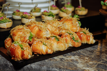 Luxury croissant canapes with crispy onions and sesame seeds on dark wooden tray.