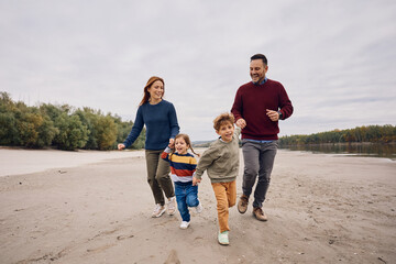 Carefree family holding hands while running during autumn day in nature.